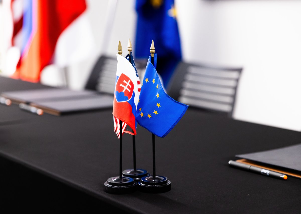 Small Slovak, United States, and European Union flags on a conference table with notebooks and pens