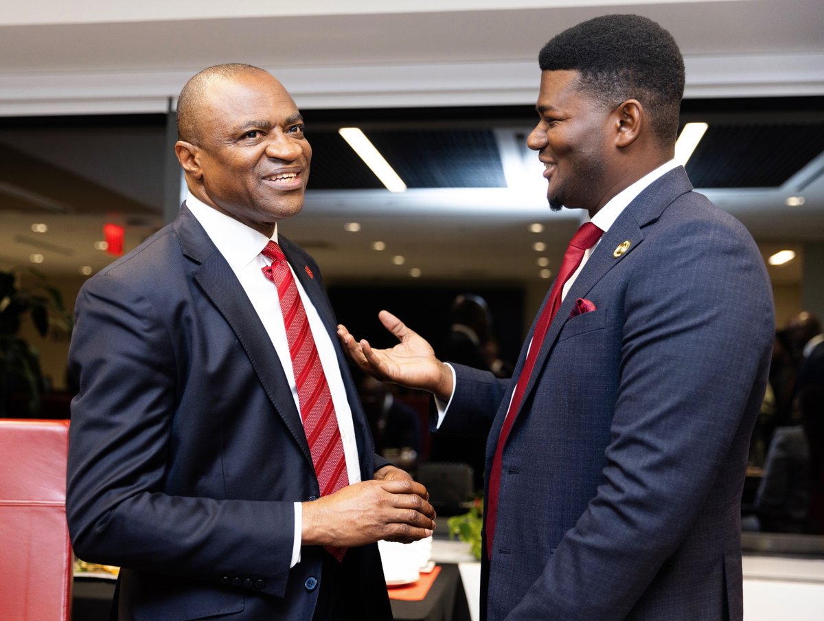 Two guests in dark suits and red ties smiling and talking at an indoor event
