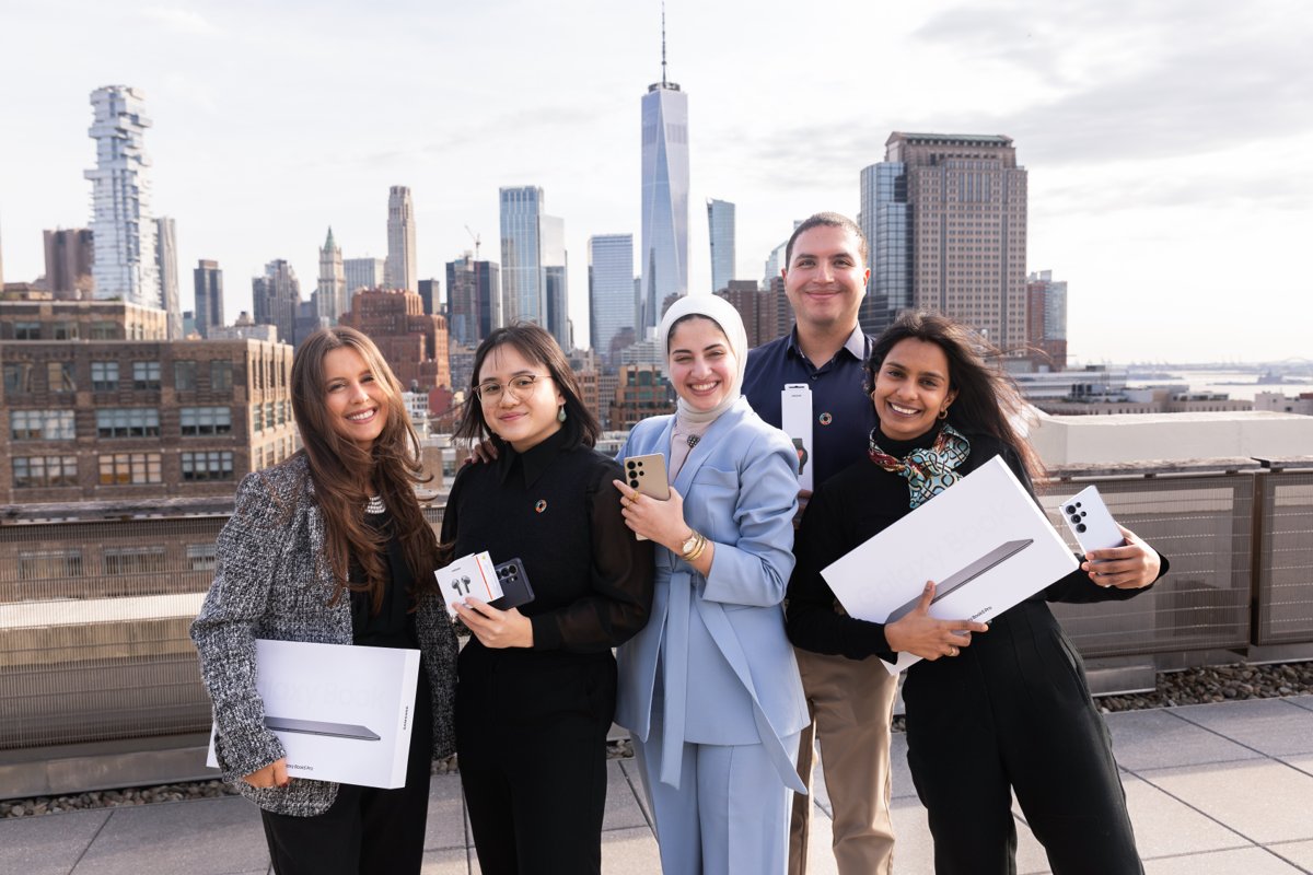 Five people holding gifts on a rooftop overlooking the New York City skyline