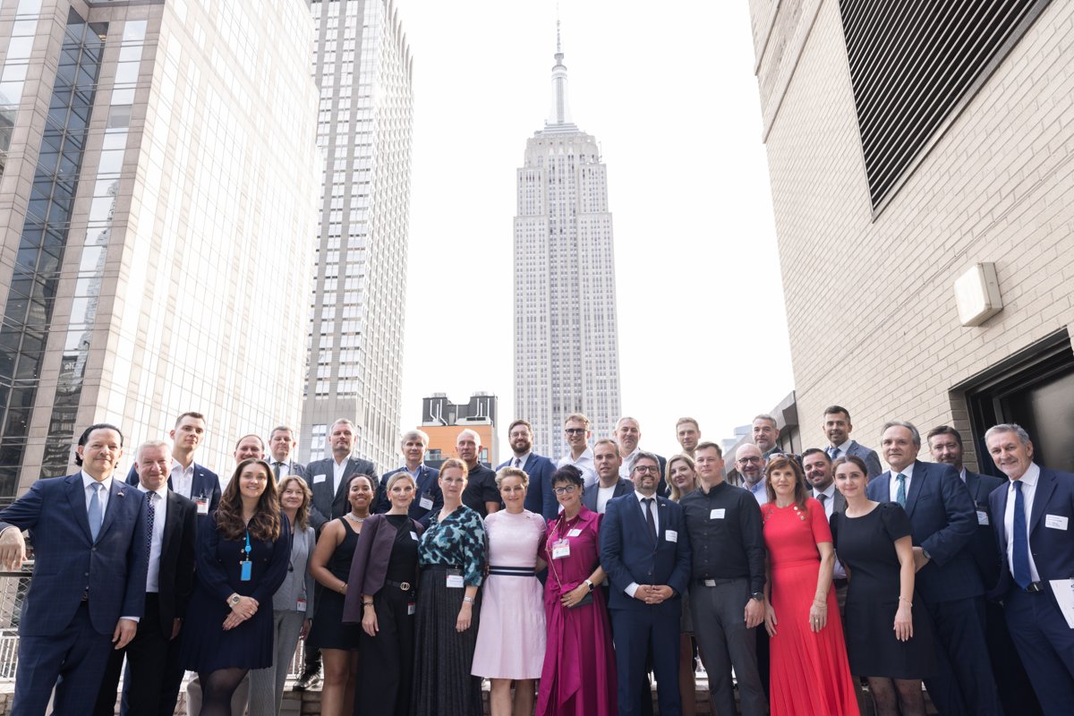 A group of attendees posing on a rooftop with the Empire State Building behind them