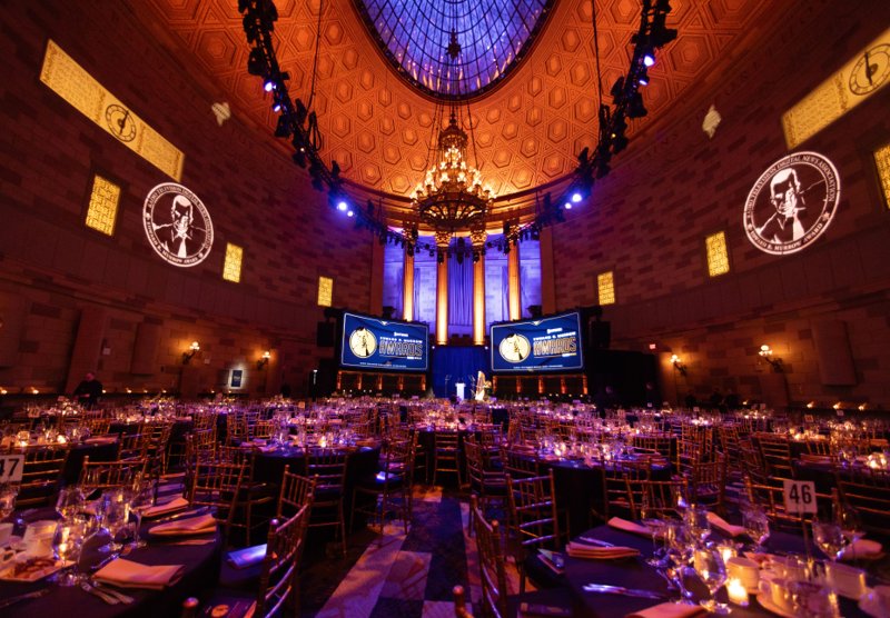 Illuminated gala ballroom with banquet tables, a chandelier and Edward R. Murrow Awards screens