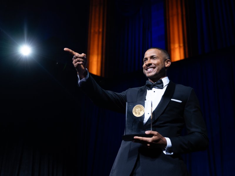 Smiling honoree pointing toward the audience while holding a Murrow Award on stage