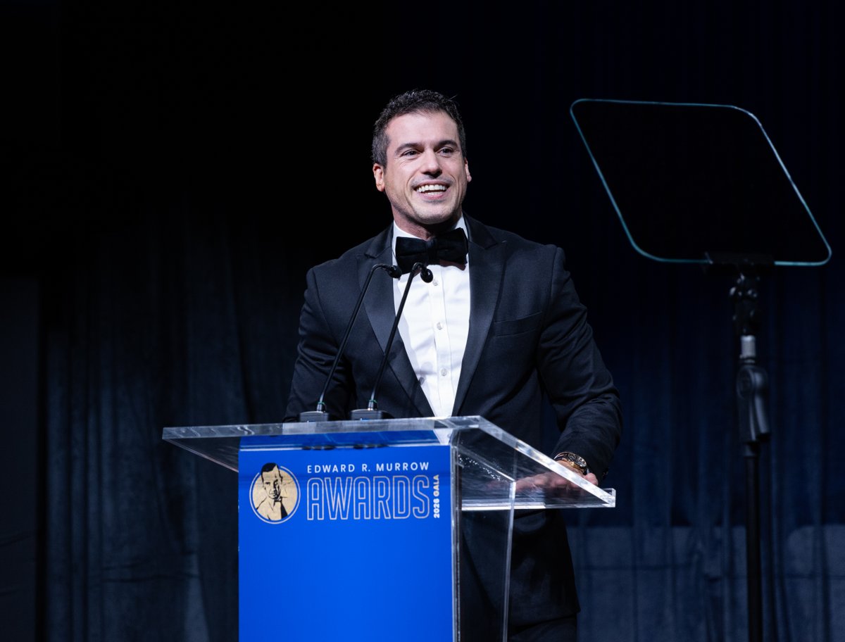 Smiling speaker in a black tuxedo at a clear lectern with an Edward R. Murrow Awards Gala sign