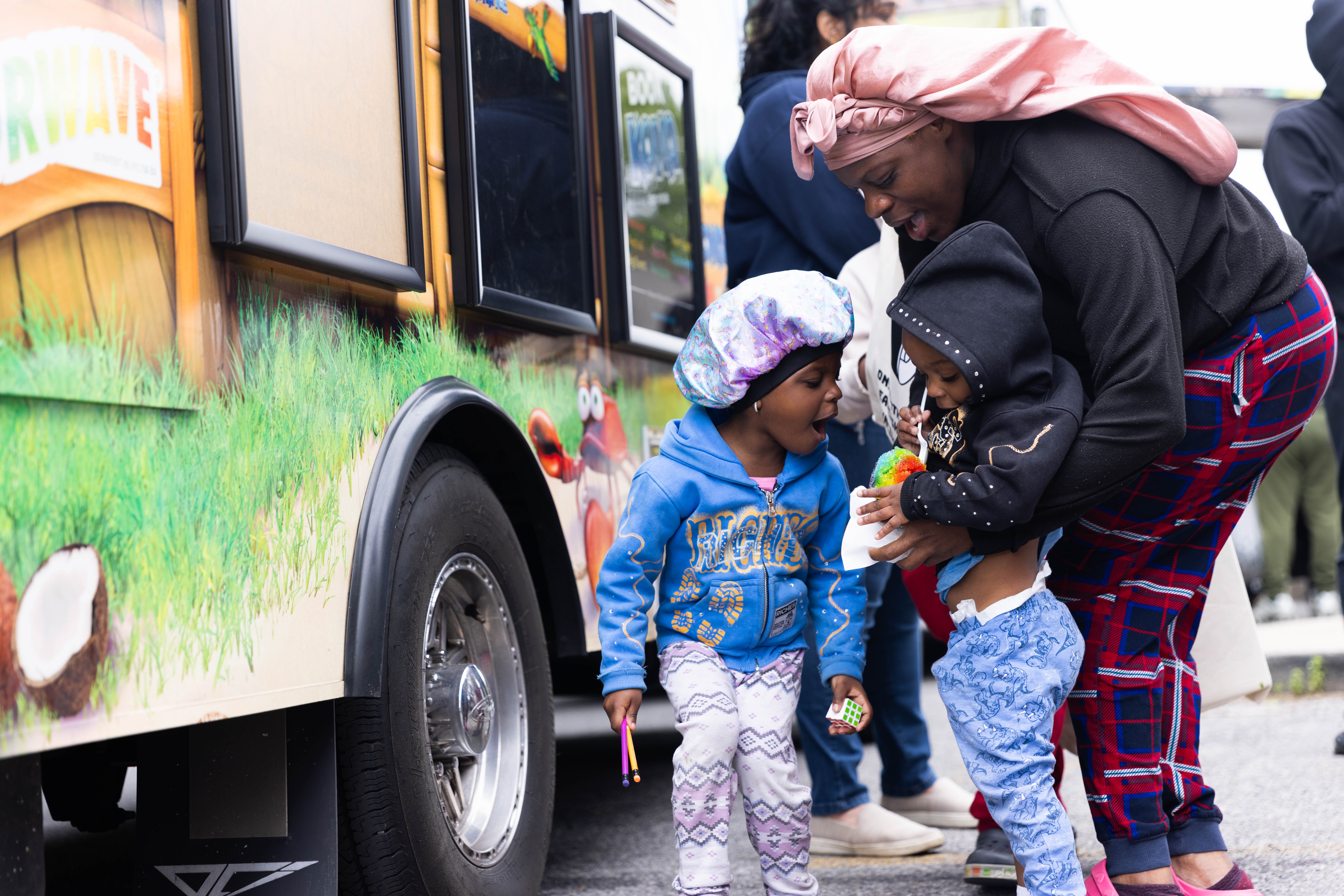 A mother helping her young children beside a colorful food truck